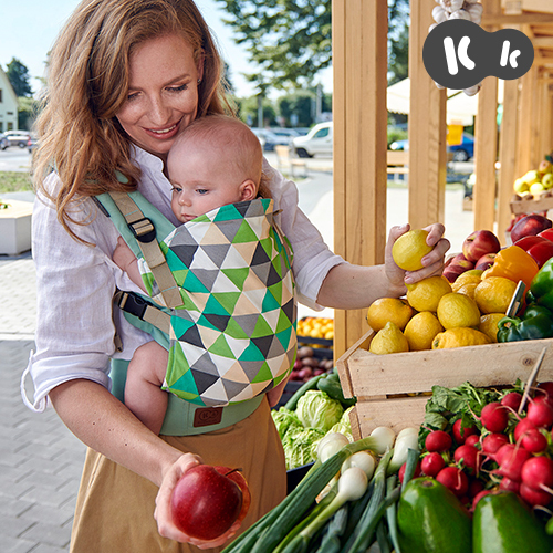 Maman portant son bébé avec le porte-bébé NINO Kinderkraft pour faire les marché