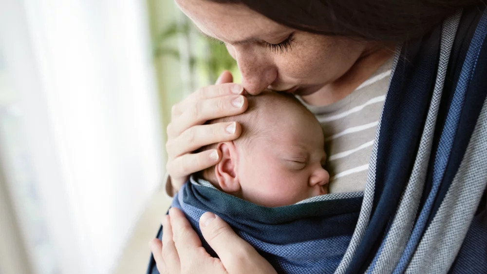 Une maman faisant un bisou à son bébé porté en écharpe de portage