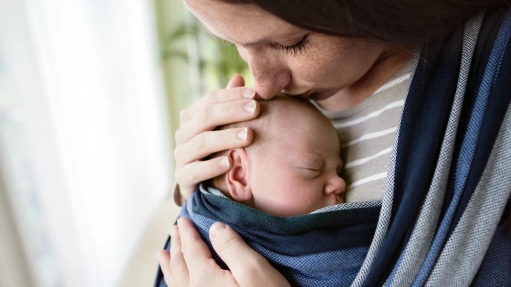 Une maman faisant un bisou à son bébé porté en écharpe de portage